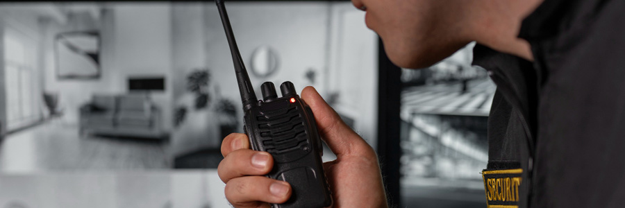 Sicherheitsmitarbeiter spricht ins Funkgerät vor Monitoren